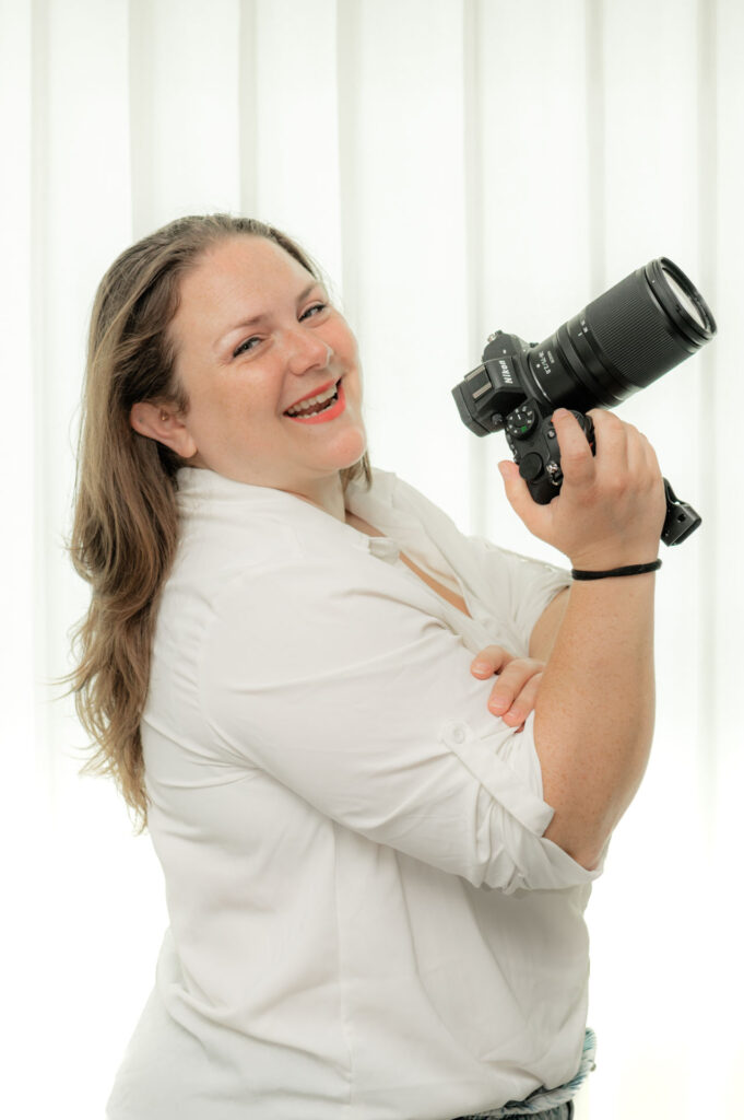 Headshot of Magenta Flute holding her camera in front of a soft white backdrop.